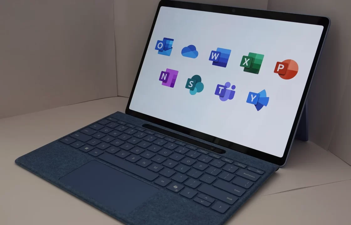 A Microsoft Surface with keyboard, its screen showing Microsoft 365 app icons including Outlook and OneDrive